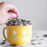 Man eating sunflower seeds from cup on table
