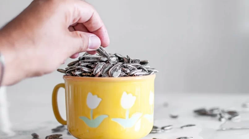 Man eating sunflower seeds from cup on table