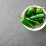 A white bowl filled with bright green jalapeno peppers